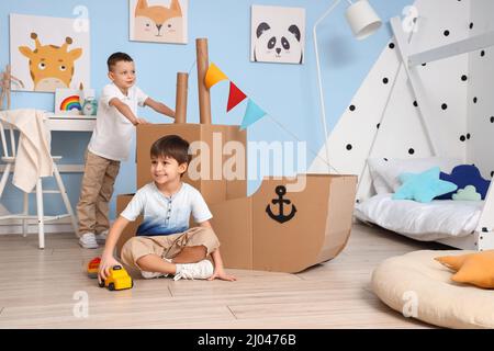 Funny little boys playing with cardboard ship at home Stock Photo