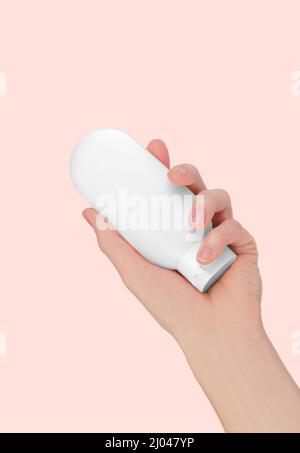 Skin care concept. Woman's hand holding white cosmetic tube isolated on pink background, mockup. Cosmetic branding mockup. Stock Photo