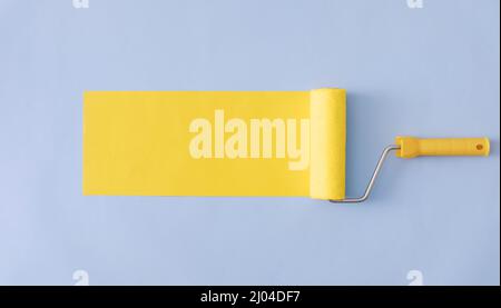 Yellow painted banner with paint roller and copy space over a blue background in a wide angle panorama Stock Photo