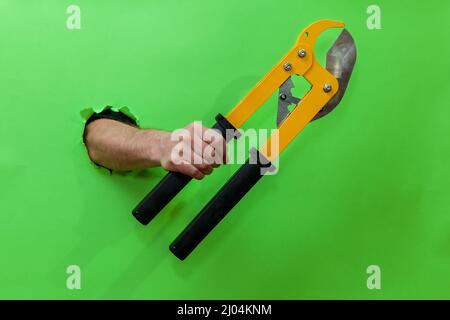 A man holds a tool for cutting plastic pipes on a green background Stock Photo