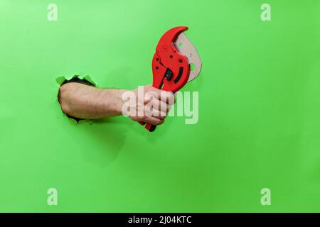 A man holds a tool for cutting plastic pipes on a green background Stock Photo