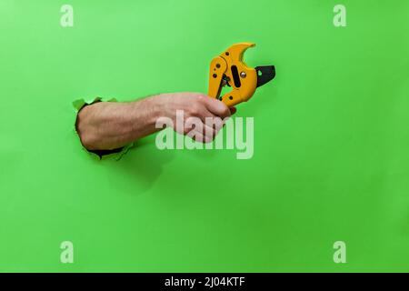 A man holds a tool for cutting plastic pipes on a green background Stock Photo