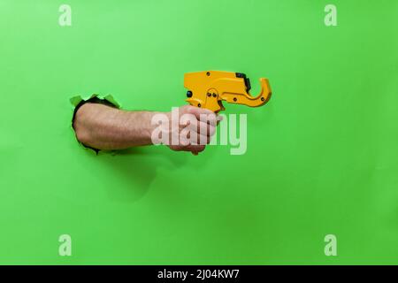 A man holds a tool for cutting plastic pipes on a green background Stock Photo