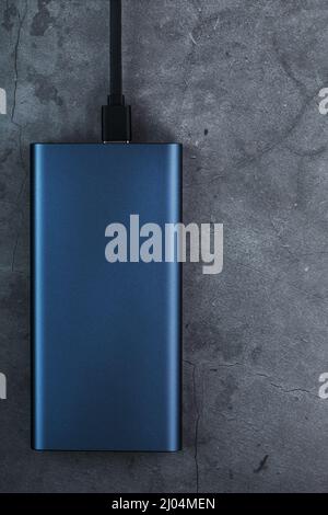 Portable External Battery Power Bank blue with USB Cord on a dark textured background for charging Gadgets Stock Photo