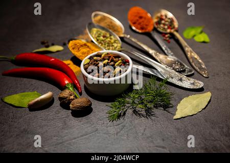 Culinary condiments. Various herbs and spices with old metal spoons on a dark background. Nutmeg, chili peppers Stock Photo