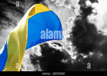 Sunlight flag of Ukraine waving on black and white sky with danger clouds. Stop war! Stock Photo