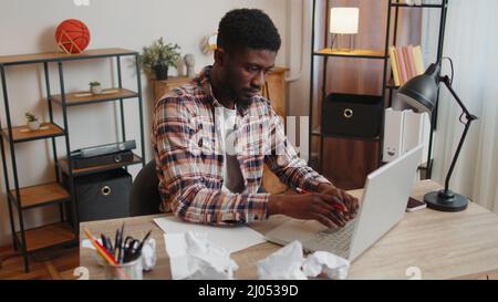 Tired man at home office falling asleep on table with laptop computer, crumpled sheets of paper Stock Photo