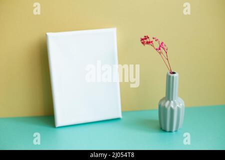 Blank canvas and dry flowers on green table. yellow wall background Stock Photo