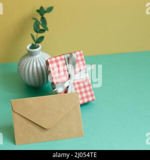 Gift box, plant, envelope on green table. yellow wall background Stock Photo