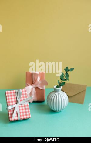 Gift box, plant, envelope on green table. yellow wall background Stock Photo