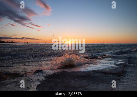 Sunset on the sea with breaking waves at pier Stock Photo