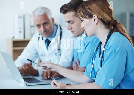 Important medical meeting in progress. Shot of three medical professionals having a discussion over a laptop. Stock Photo