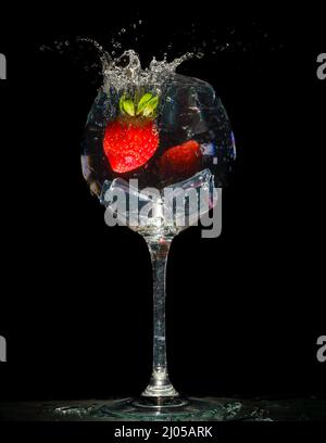 Ripe red strawberry in a glass with water and splashes on a black background with copy space. Stock Photo