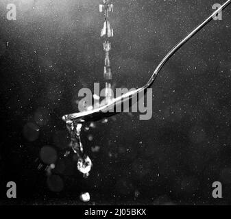 Water pours on a spoon and splashes on the sides with a dark background with soft bokeh and glitter Stock Photo