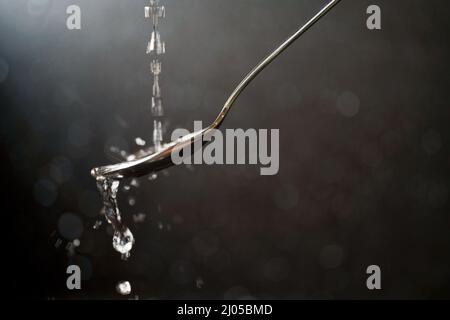 Water pours on a spoon and splashes on the sides with a dark background with soft bokeh and glitter Stock Photo