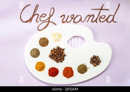 Chef wanted handwritten on purple paper with brown chalk, next to a painter's palette with condiments as painting colors (paprika, curcuma, all spice, Stock Photo