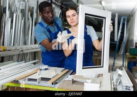 Portrait of man and woman worker who are standing with window frames in the pvc workshop. Stock Photo