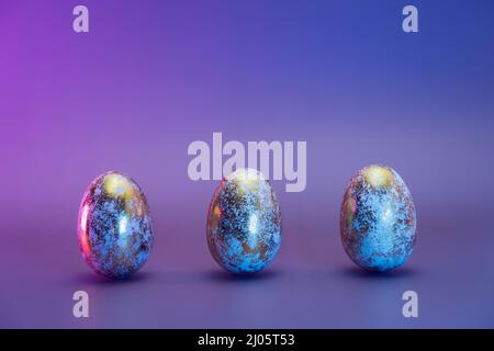 Row of three Easter golden eggs with different patterns in neon colors light. Purple very peri color minimalist festive background. Modern trendy East Stock Photo