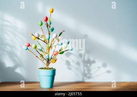 Easter tree decor in blue pot with colorful eggs on the wooden console with light and shadow background. Easter holiday home decoration. Minimalism, s Stock Photo