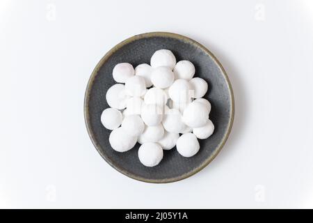 White sugar balls in a gray ceramic plate on a white background. Close up top view. Stock Photo