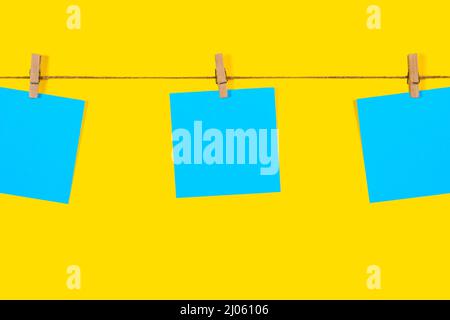 Blue Note papers and decorative pin or clip isolated on yellow background. Office mock up. Top view, flat lay. Colorful office note or sticker papers Stock Photo
