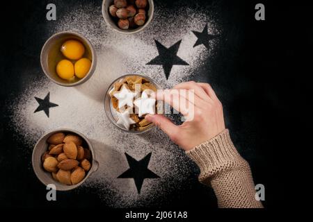 Bakery background for cooking Christmas baking with scattered flour, eggs, nuts, biscuits. Womans hand holds star shape cookie Stock Photo