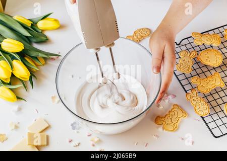 Cropped shot of woman using mixer machine making cookie icing for decoration. Woman holding glass bowl with sugar glaze and electric mixer. Easter holiday backing Stock Photo