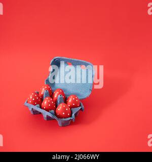 Creative Easter concept of cardboard box of eggs painted in red. Pastel red background. Stock Photo