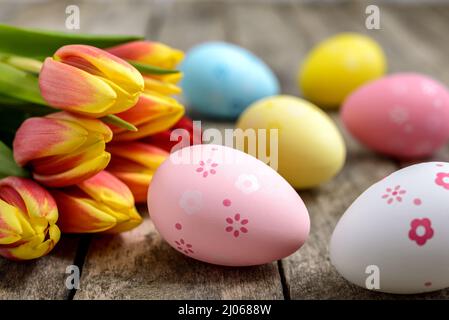 Colorful decorated Easter eggs and a bouquet of tulips on a rustic wooden table. Easter concept. Stock Photo