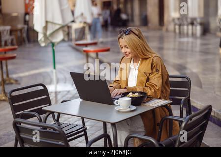 Focused woman sitting at table in street cafe, working on laptop Stock Photo