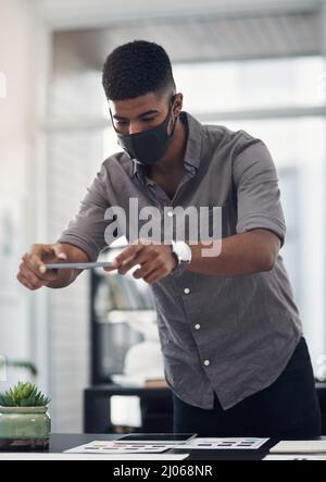 Taking photos to help him see the bigger picture. Shot of a young designer taking photos of his work in an office. Stock Photo