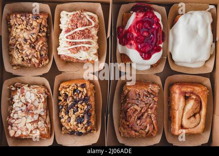 Box of assorted  fresh baked cinnamon rolls close up, flat lay. Walnut, raisin, almond, pecan, maple bacon, cream cheese toppings Stock Photo