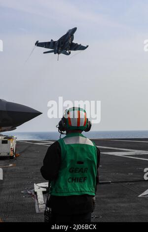 PHILIPPINE SEA (March 15, 2022) Aviation Boatswain's Mate (Equipment) 1st Class Nabil Pareja, from Richmond, Calif., observes an EA-18G Growler, assigned to the 'Wizards' of Electronic Attack Squadron (VAQ) 133, flies over the flight deck of the Nimitz-class aircraft carrier USS Abraham Lincoln (CVN 72) following a joint long-range air demonstration in the Yellow Sea, March 15. Abraham Lincoln Strike Group is on a scheduled deployment in the U.S. 7th Fleet area of operations to enhance interoperability through alliances and partnerships while serving as a ready-response force in support of a f Stock Photo