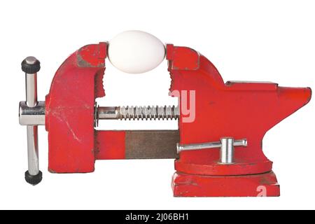 An Egg in the Jaws of a Red Metal Bench Vice Isolated on a White Background Stock Photo