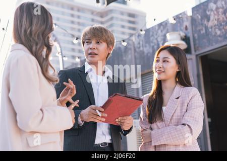 Asian business people working together and using a digital tablet. Group of professionals discussing outdoors Stock Photo