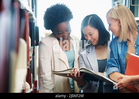 Cramming some last minute knowledge. Young people standing in the library and looking at a book together. Stock Photo