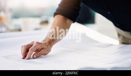 Attention to detail is vital in his line of business. Shot of an unrecognizable architect working on a blueprint in his office. Stock Photo