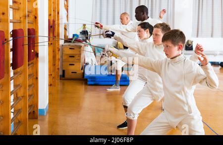 Children with adults practicing effective techniques of fencing in gym Stock Photo