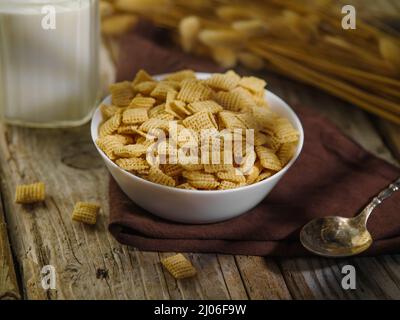 Close-up. A bowl of cereal flakes, a spoon, a jug of milk and a bunch of flakes on a wooden background, a brown napkin. Quick breakfast cereals, healt Stock Photo