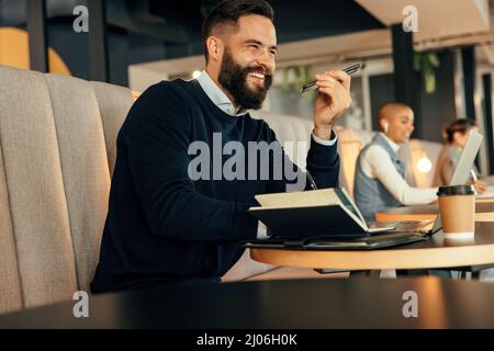Cheerful businessman making notes during a phone call. Young businessman smiling happily while making plans with his associates over the phone. Modern Stock Photo