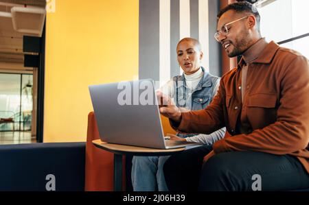 Cheerful business colleagues having a discussion in an office lobby. Two young entrepreneurs using a laptop in a co-working space. Two young businessp Stock Photo
