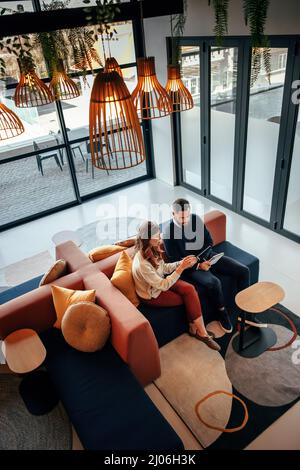 Top view of two businesspeople working in an office lobby. Two modern businesspeople using a digital tablet while having a discussion. Two young entre Stock Photo