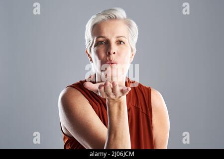 Sending love and kisses to the whole world. Portrait of an attractive mature woman blowing kisses against a grey background. Stock Photo