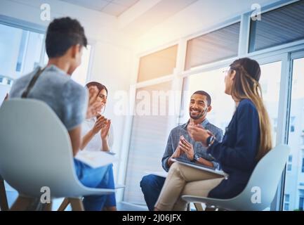 He deserves a round of applause. Shot of a group of cheerful young businesspeople having a creative meeting at work. Stock Photo