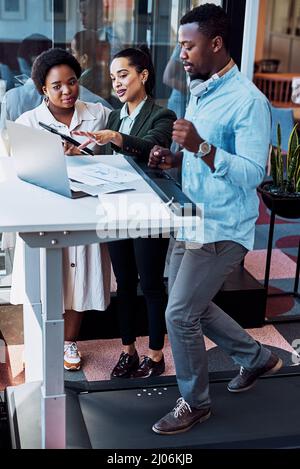 Getting all their creative juices flowing. Shot of a businessman walking on treadmill while having a meeting with his colleagues in an office. Stock Photo