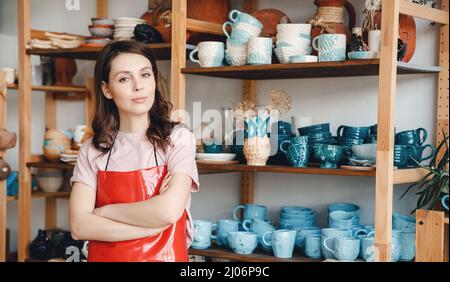 Confident young woman standing in an apron for pottery wheel. Concept of opening your own business. Stock Photo