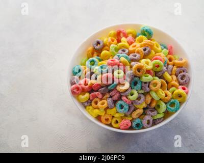 Crispy multi-colored corn rings in a bowl on a white background. Close-up. Quick breakfast cereals, vitamins, healthy food, baby food. Stock Photo