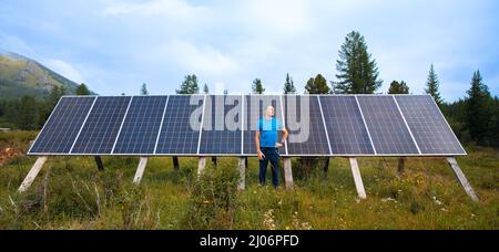 Autonomous housing, man farmer stands against backdrop of solar panels to generate electricity. Concept life in mountains of Iceland and Russia. Stock Photo