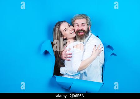 Couple through hole in blue paper. Discount and sale, people hole background. Surprised couple of man and woman making hole in paper looking through Stock Photo