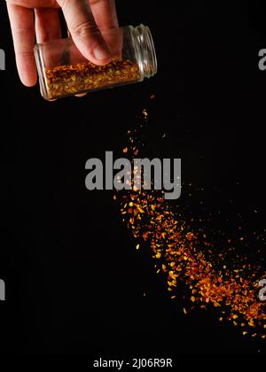 A jar of seasonings, spices in a female hand. Spices in frozen flight isolated on black background. Black and gold colors. Cafe, restaurant, hotel, su Stock Photo